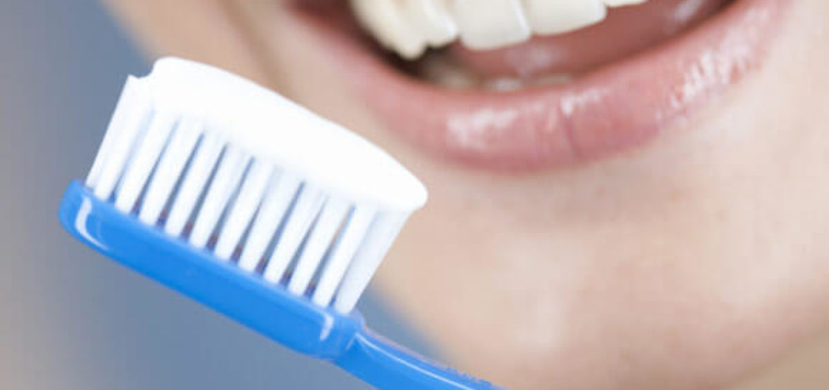 Toothbrush with toothpaste ready to brush with smiling woman in background